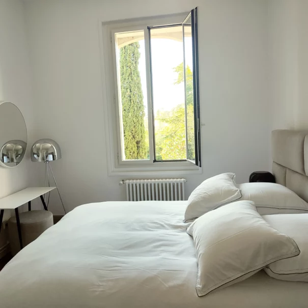 Un lit queen size et un mobilier simple et élégant dans la chambre numéro 1 de la Bastide Castella, une fenêtre donne sur le parc
