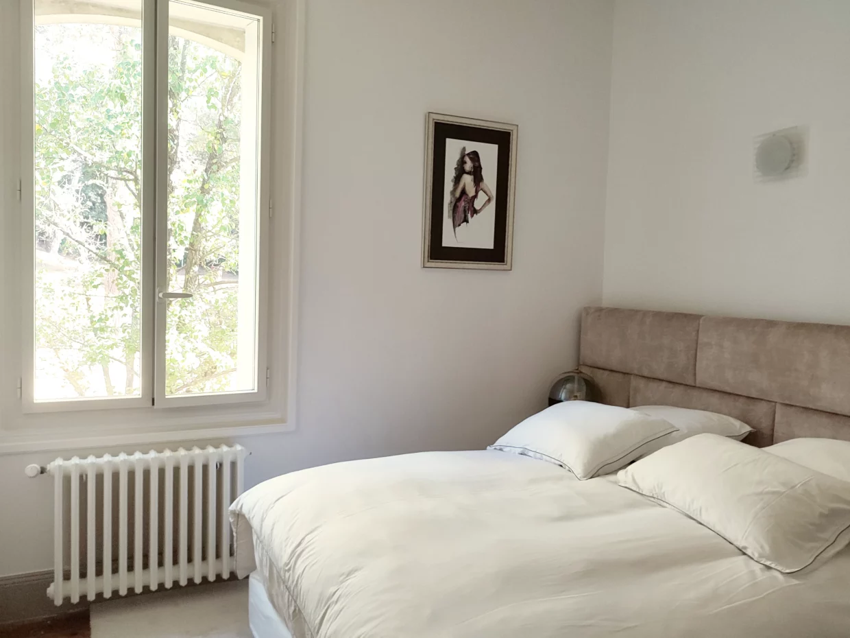 Un lit queen size dans la chambre numéro 3 de la Bastide Castella, une fenêtre donne sur le parc.